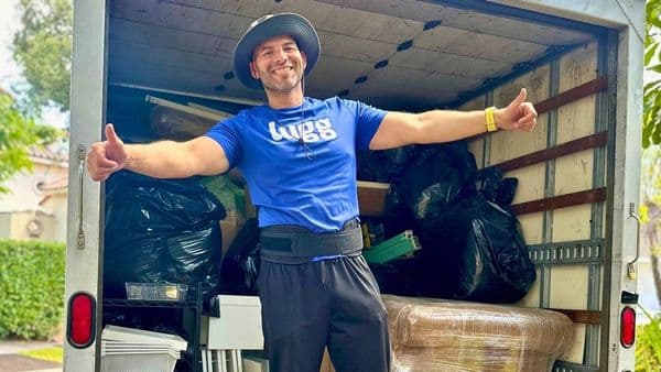 A Lugg mover standing in front of a Lugg box truck packed full with a complete home's worth of furniture, boxes, and household items mid-move outside a single-family home.