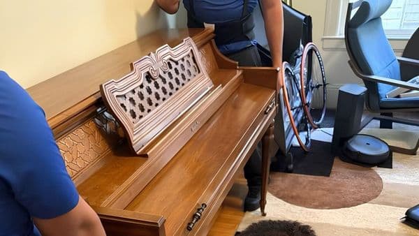 Two Lugg movers carefully positioning a wood upright piano in a customer's living room during a residential piano move.